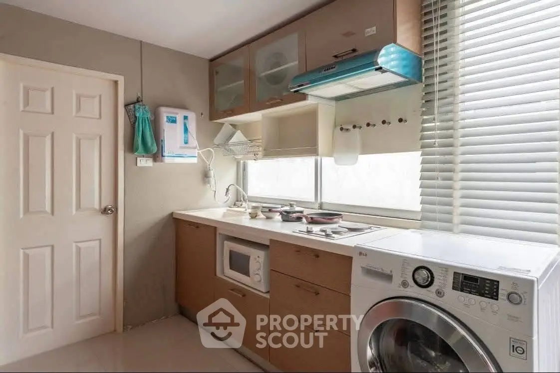 Modern kitchen with washing machine and microwave, featuring sleek cabinetry and ample natural light.