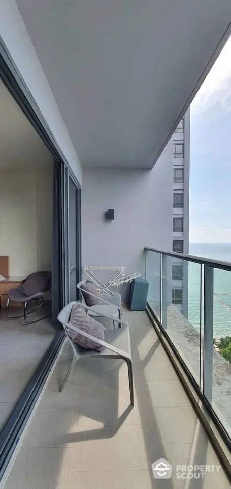 Modern balcony with ocean view, glass railing, and cozy seating area.