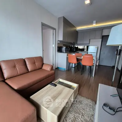 Modern living room with brown leather sofa and open kitchen layout in stylish apartment.