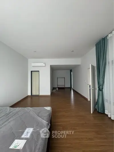 Spacious bedroom with wooden flooring and natural light, featuring a modern air conditioning unit and elegant curtains.