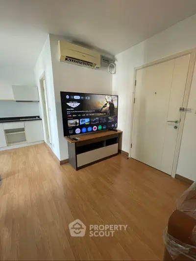 Modern living room with wooden flooring, wall-mounted air conditioner, and large flat-screen TV.