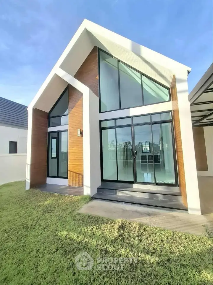 Modern house exterior with large glass windows and sloped roof design.