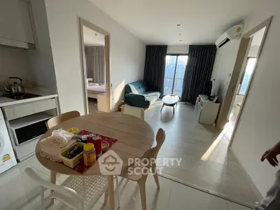 Modern open-plan apartment with kitchen, dining area, and living room featuring natural light and contemporary decor.