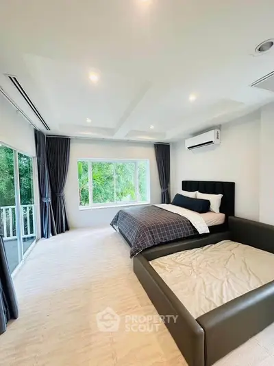 Spacious bedroom with large windows and modern decor, featuring a serene view of greenery.