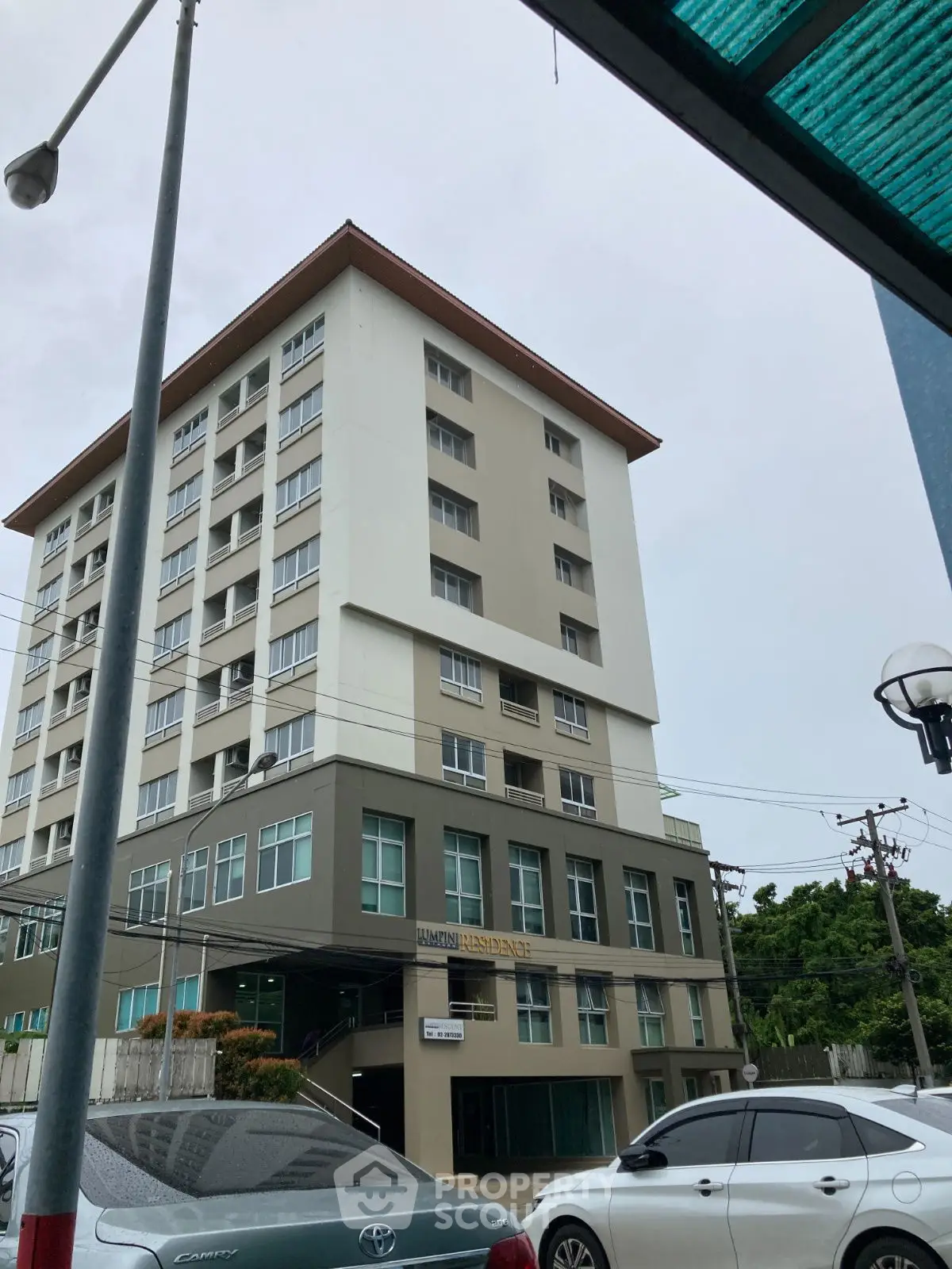 Modern multi-story residential building with parking area and street view.
