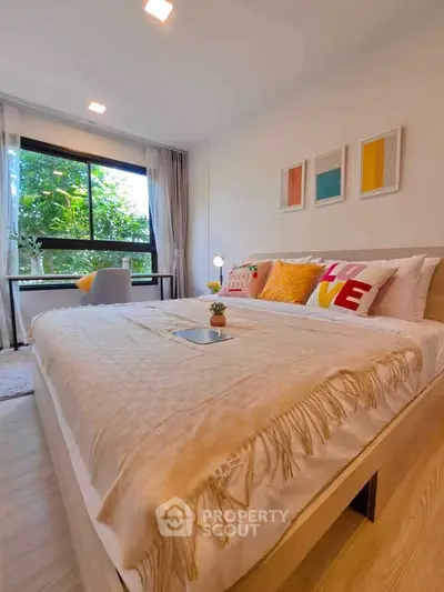 Spacious bedroom with large window and modern decor, featuring a cozy bed and vibrant pillows.