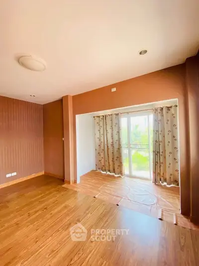 Spacious empty room with wooden flooring and large window for natural light