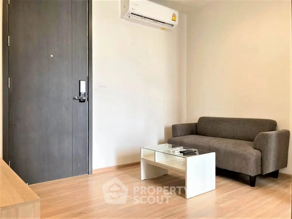 Modern living room with sleek sofa and glass coffee table, featuring minimalist design and air conditioning.