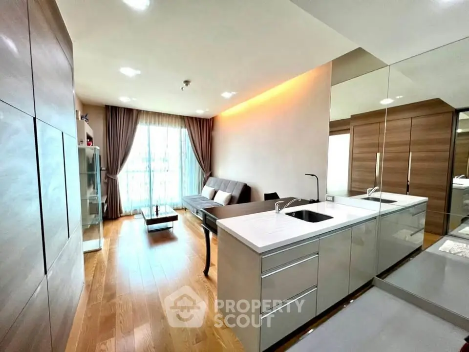 Modern open-plan living room with sleek kitchen, hardwood floors, and large windows for natural light.