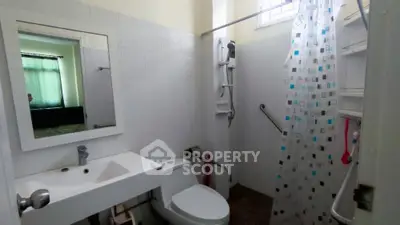Compact and functional bathroom with white fixtures, shower curtain, and a small window for natural light, ideal for urban living.