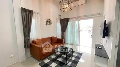 Modern living room with leather sofa, stylish chandelier, and wall-mounted TV in a bright, airy space.