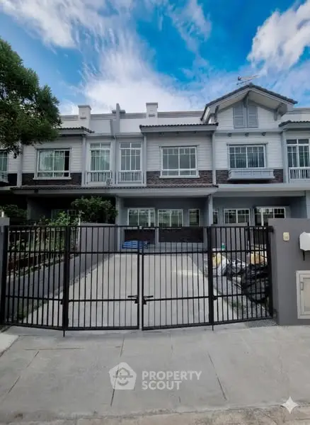 Charming townhouse with gated driveway and modern facade under a bright blue sky.