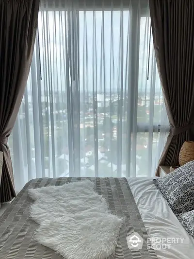 Cozy bedroom with large window offering stunning city view and elegant curtains