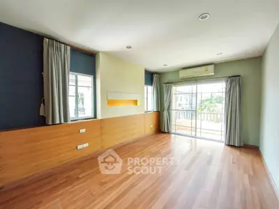Spacious living room with wooden flooring and large windows opening to a balcony, perfect for natural light.