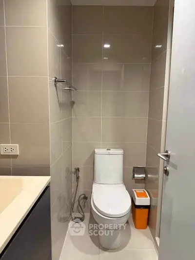 Modern bathroom with sleek design and neutral tiles, featuring a toilet and bidet spray.