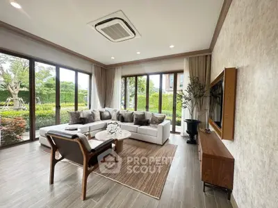 Spacious living room with modern decor and garden view, featuring large windows and elegant furniture.