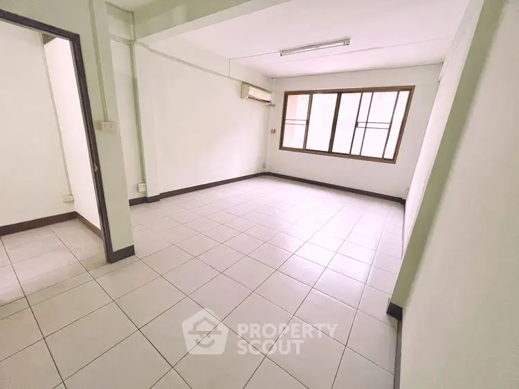 Spacious empty room with large window and tiled floor, perfect for customization.