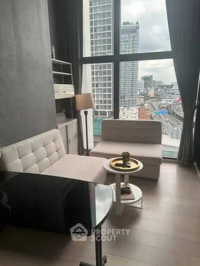 Modern living room with large windows offering city views, featuring stylish furniture and elegant decor.