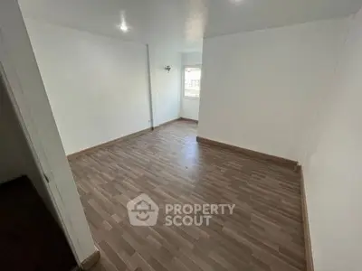 Spacious empty room with wooden flooring and bright natural light.