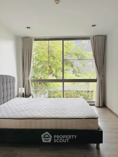 Spacious bedroom with large window and garden view, featuring a modern bed and elegant curtains.