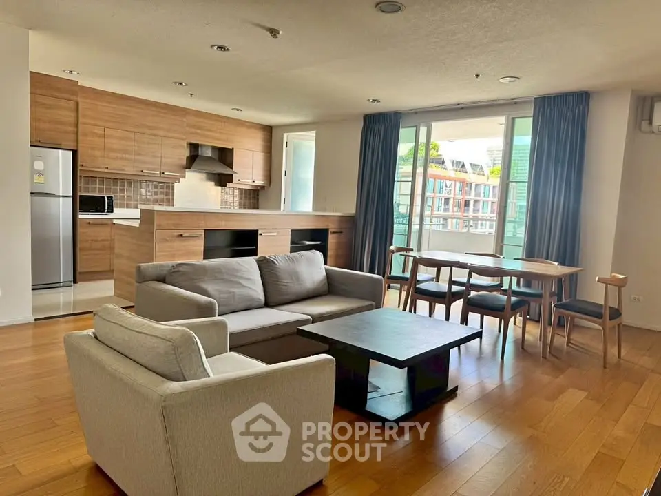 Spacious open-plan living room with modern kitchen and dining area, featuring wooden flooring and ample natural light.