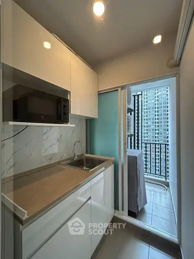 Modern compact kitchen with sleek cabinetry and balcony view in urban apartment