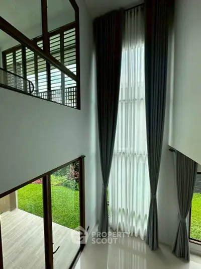 Spacious modern living room with high ceilings and large windows overlooking a lush garden.