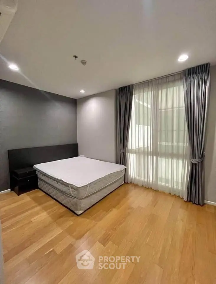 Spacious bedroom with wooden flooring and large window in modern apartment