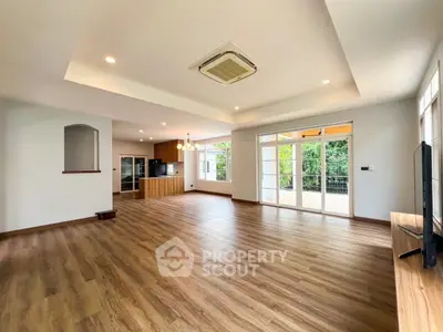 Spacious open-plan living room with wooden flooring and large windows overlooking greenery.