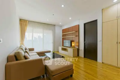 Modern living room with cozy sofa and entertainment center, featuring wooden flooring and large window.