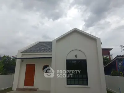 Charming modern house with unique circular window and wooden door under cloudy sky.
