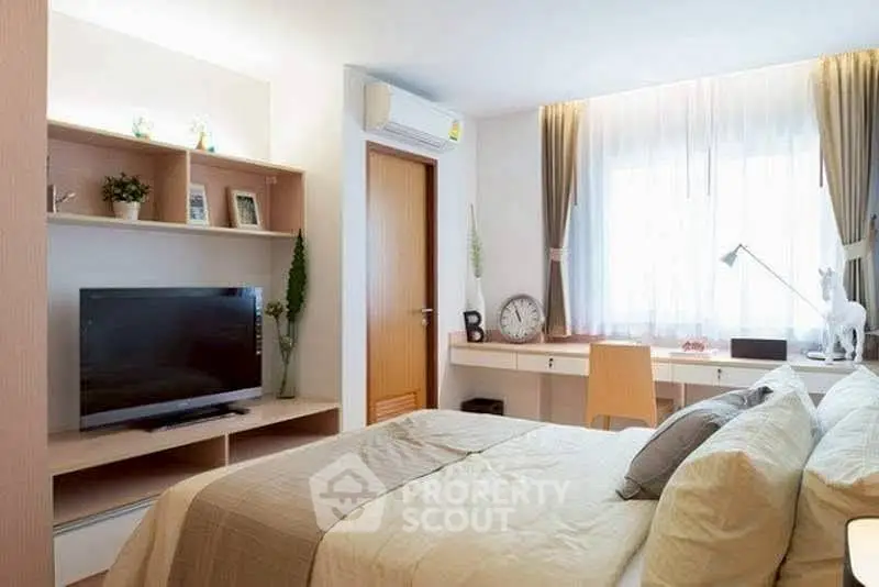 Cozy modern bedroom with stylish decor and natural light, featuring a TV and workspace.