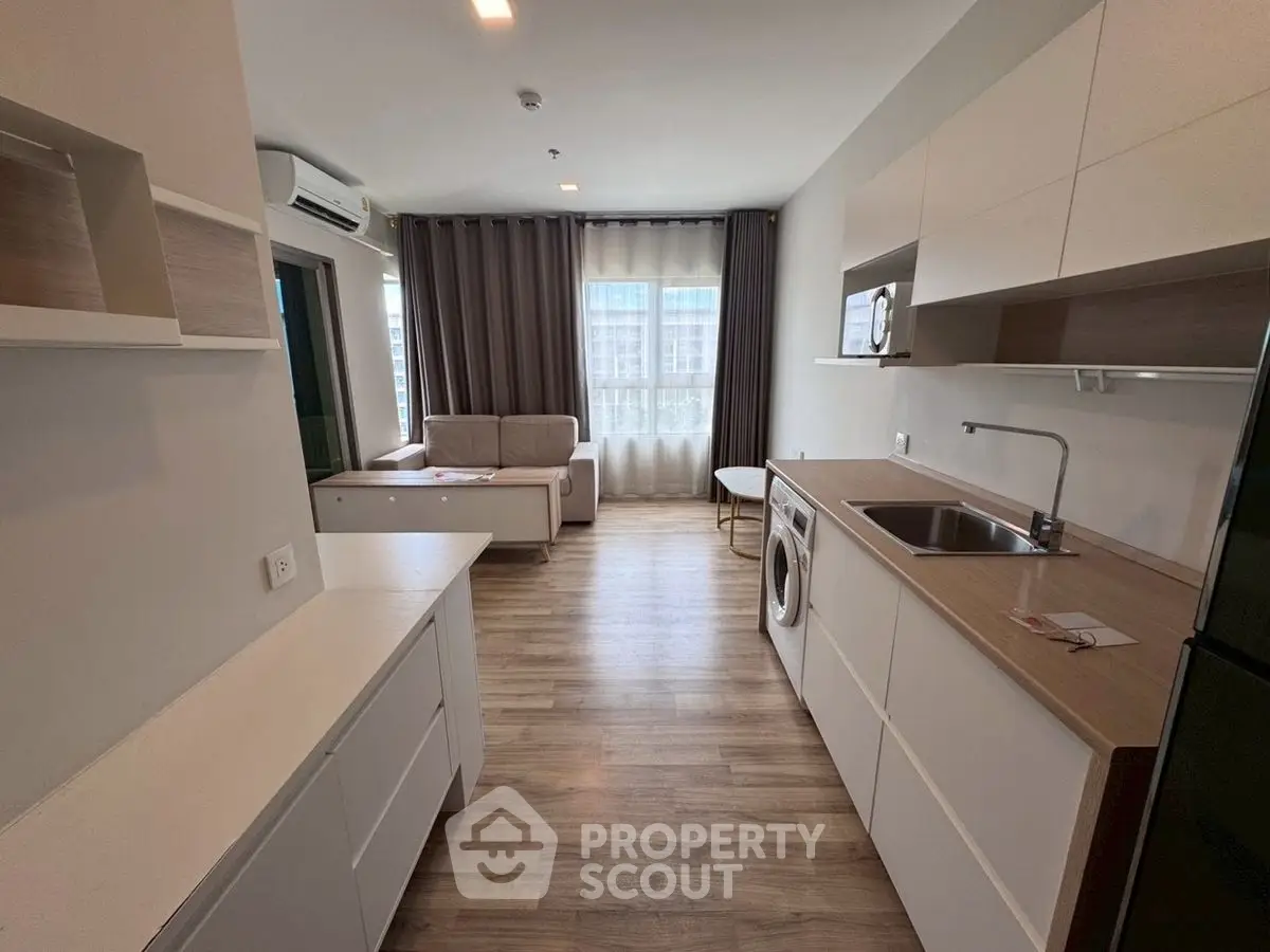 Modern open-layout living room with kitchen, featuring sleek design and natural light.