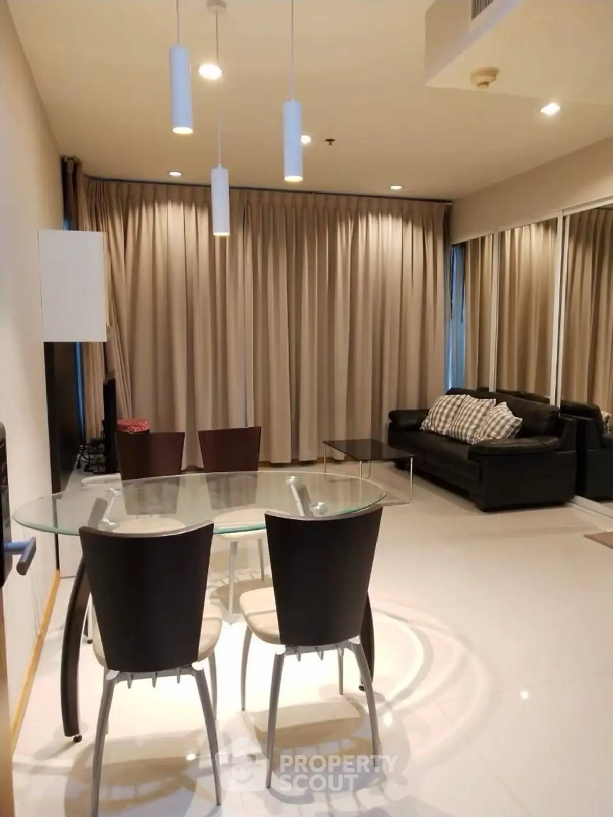 Modern living room with glass dining table and leather sofa, featuring elegant lighting and floor-to-ceiling curtains.