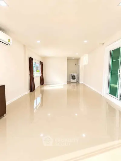 Spacious living room with large windows and washing machine, perfect for modern living.