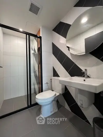 Modern bathroom with sleek black and white tiles, glass shower, and round mirror.