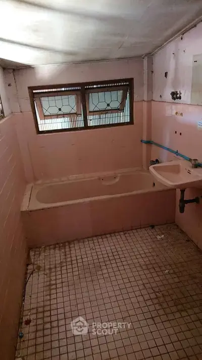 Vintage pink-tiled bathroom with bathtub and small windows, ideal for renovation.