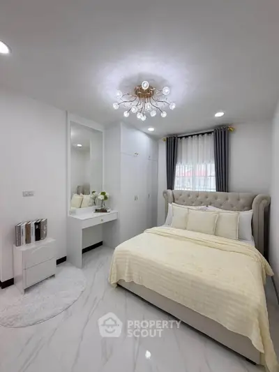 Elegant bedroom with plush bed, modern chandelier, and sleek white decor.