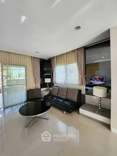 Modern living room with sleek black sofa and large windows for natural light.