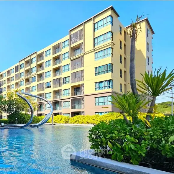 Modern apartment building with pool and lush greenery under clear blue sky.