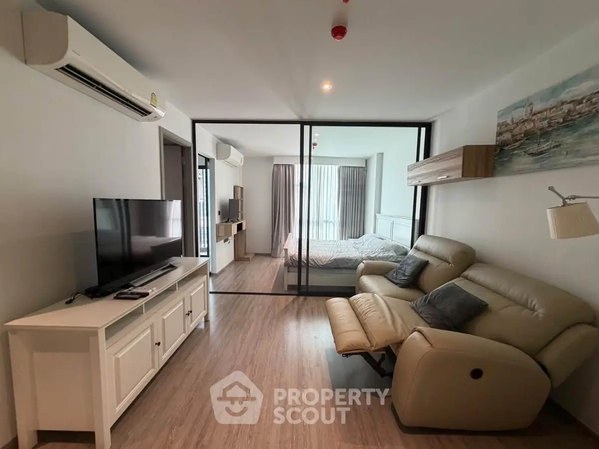 Modern living room with sleek design and glass partition leading to bedroom, featuring cozy seating and stylish decor.