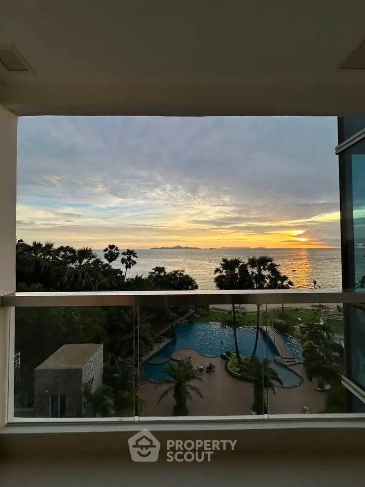 Stunning ocean view from a modern balcony overlooking a pool and lush greenery at sunset.