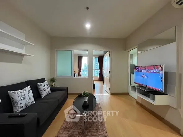 Modern living room with sleek black sofa, wall-mounted TV, and stylish decor in a cozy apartment.
