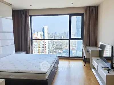 Modern bedroom with city view, featuring large window, bed, and desk in high-rise apartment.