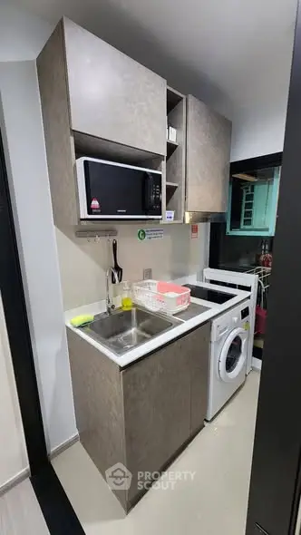 Compact modern kitchen with microwave and washing machine in small apartment.
