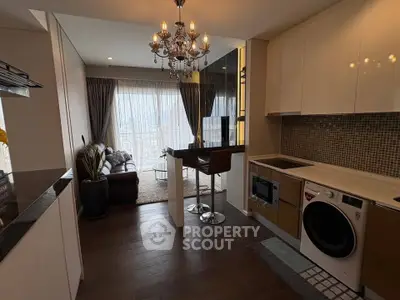 Modern open-layout kitchen with chandelier and cozy living area, featuring a washing machine and elegant decor.
