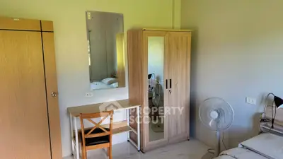 Cozy bedroom with wooden furniture, mirror, and fan, perfect for a comfortable living space.