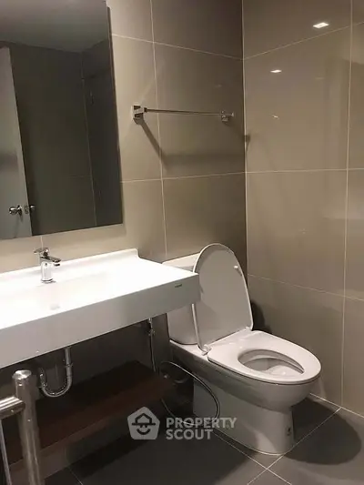 Modern bathroom with sleek fixtures and neutral tiles, featuring a contemporary sink and toilet.