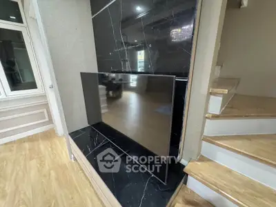 Modern living room with sleek black marble TV wall and wooden staircase