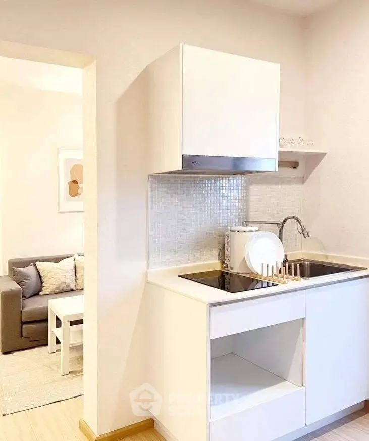 Modern compact kitchen with sleek white cabinetry and cozy living room view.